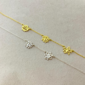 K&ouml;nnte beinhalten: Zwei zarte Halsketten mit floralem Design. Eine Halskette ist golden, die andere silbern. Beide Halsketten haben mehrere Blumenanh&auml;nger.