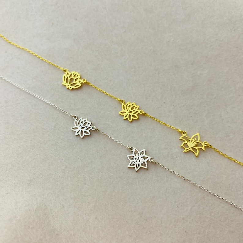 K&ouml;nnte beinhalten: Zwei zarte Halsketten mit floralem Design. Eine Halskette ist golden, die andere silbern. Beide Halsketten haben mehrere Blumenanh&auml;nger.