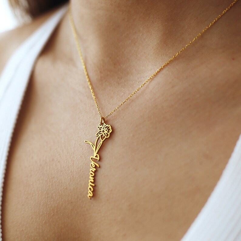 May include: A gold necklace with a delicate daffodil pendant and the name "Veronica" inscribed on the stem.