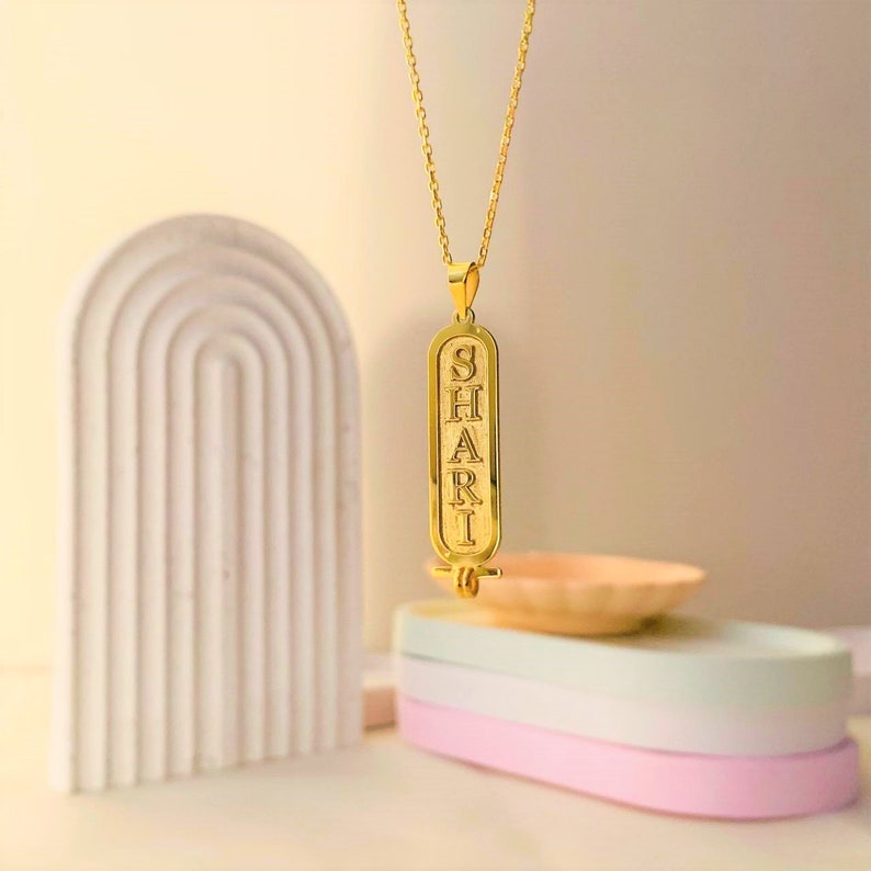 K&ouml;nnte beinhalten: Goldkette mit einem Anh&auml;nger, auf dem das Wort "SHARI" in einem alten &auml;gyptischen Hieroglyphenstil eingraviert ist.