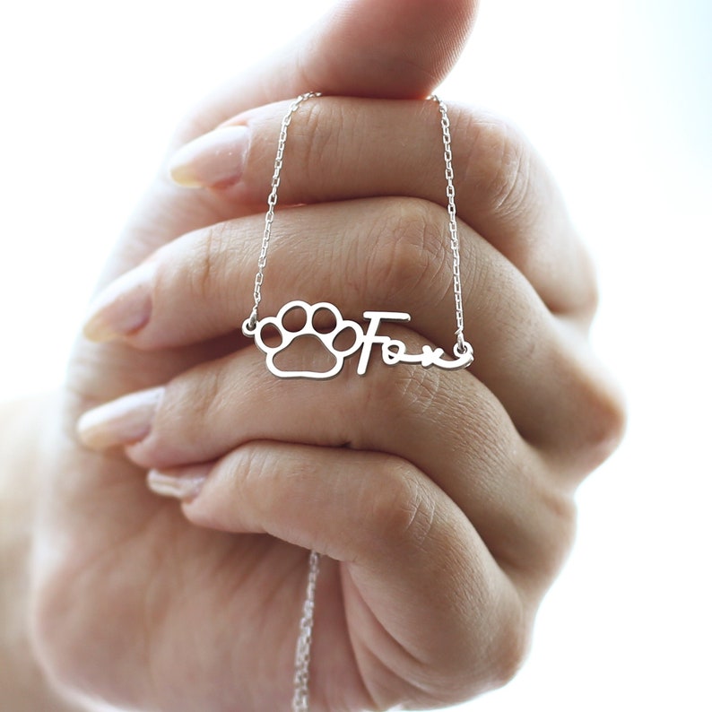 May include: Silver necklace with a paw print charm and the name "Fox" written in cursive.