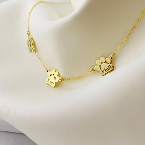 May include: Gold necklace with three paw print charms, each engraved with a name: Kim, Phil, and a third name that is partially obscured.