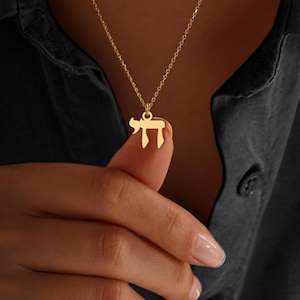Peut inclure: Un collier dor&eacute; avec un pendentif en forme de la lettre h&eacute;bra&iuml;que 'Chai'. Le pendentif est suspendu &agrave; une cha&icirc;ne d&eacute;licate. Le collier est pr&eacute;sent&eacute; sur un fond sombre.
