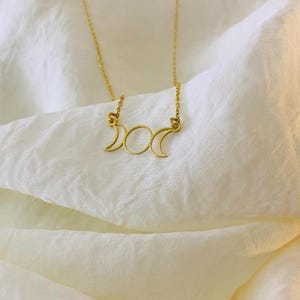K&ouml;nnte beinhalten: Eine goldene Halskette mit einem dreifachen Mond-Anh&auml;nger. Der Anh&auml;nger ist ein schlichtes Design mit drei Mondsicheln.