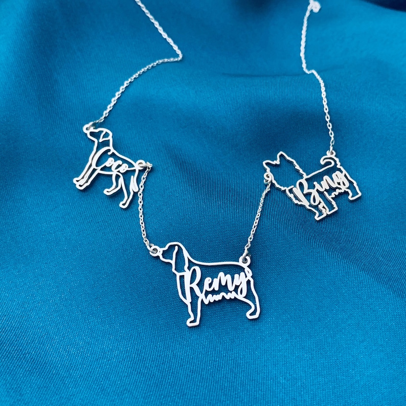 May include: A silver necklace with three dog silhouettes, each with a name inscribed inside. The names are "Coco", "Remy", and "Bingo".