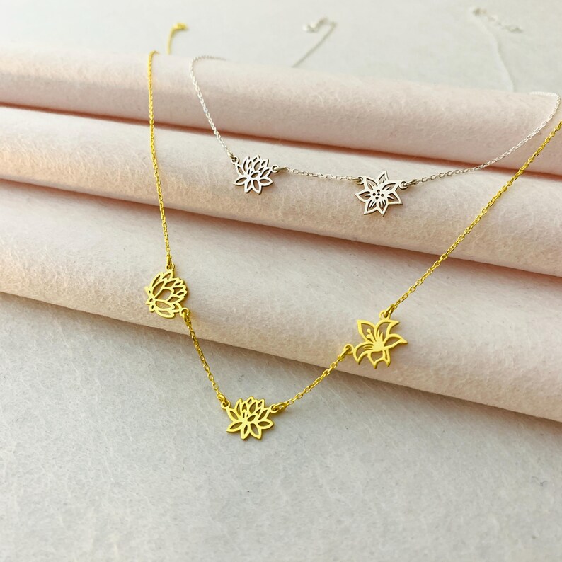 K&ouml;nnte beinhalten: Zwei zarte Halsketten mit mehreren Blumenanh&auml;ngern. Eine Halskette ist golden mit drei Blumenanh&auml;ngern, die andere ist silber mit zwei Blumenanh&auml;ngern.