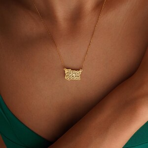 May include: A gold-coloured necklace featuring the words "Silence not an Option" in a decorative font. The pendant is suspended from a fine chain. The necklace is worn against the skin, with a green top visible.
