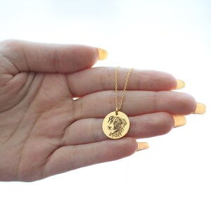 May include: A gold pendant necklace with a detailed engraved image of a dog's face. The round pendant has the dog's name, "Ryder," engraved below the image. The necklace chain is fine and gold-coloured.