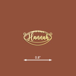 May include: Gold-coloured metal football charm with the name "Hannah" inscribed on it. The charm is 0.8 inches in diameter.