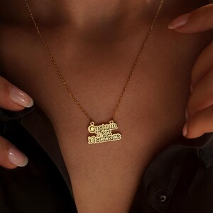 May include: A gold-colored necklace with the words "Custom Text Necklace" in a stylized font. The necklace is displayed against a dark background.