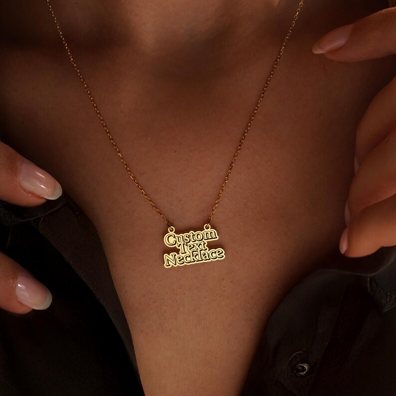 May include: A gold-colored necklace with the words "Custom Text Necklace" in a stylized font. The necklace is displayed against a dark background.