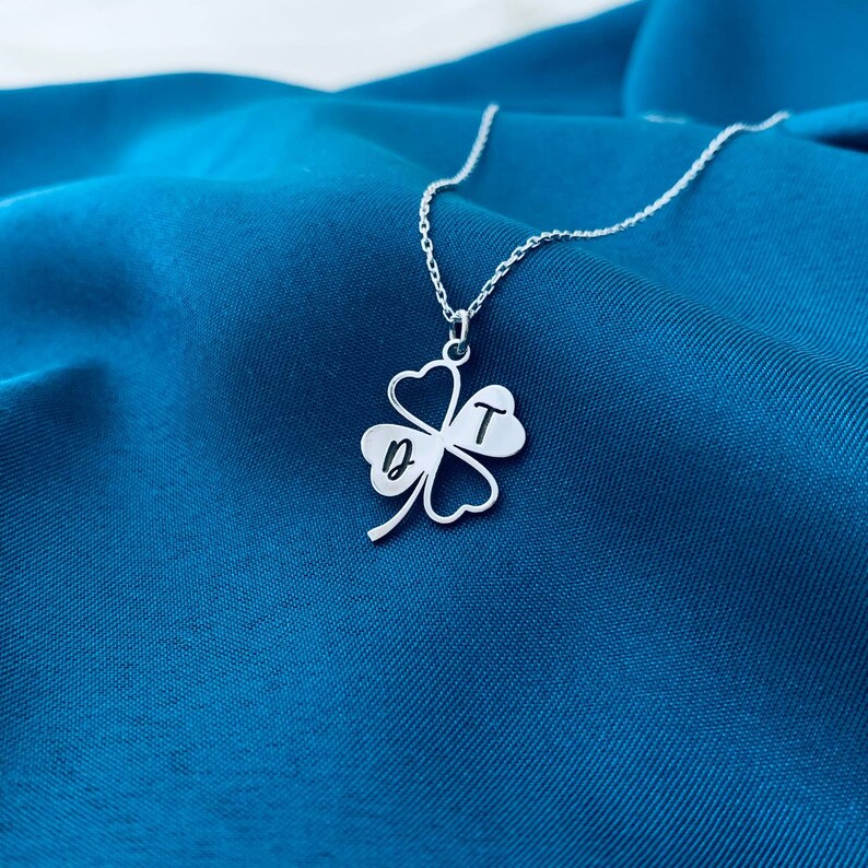 Peut inclure: Un collier en argent avec un pendentif en forme de tr&egrave;fle &agrave; quatre feuilles. Le tr&egrave;fle porte les lettres "D" et "T" grav&eacute;es.