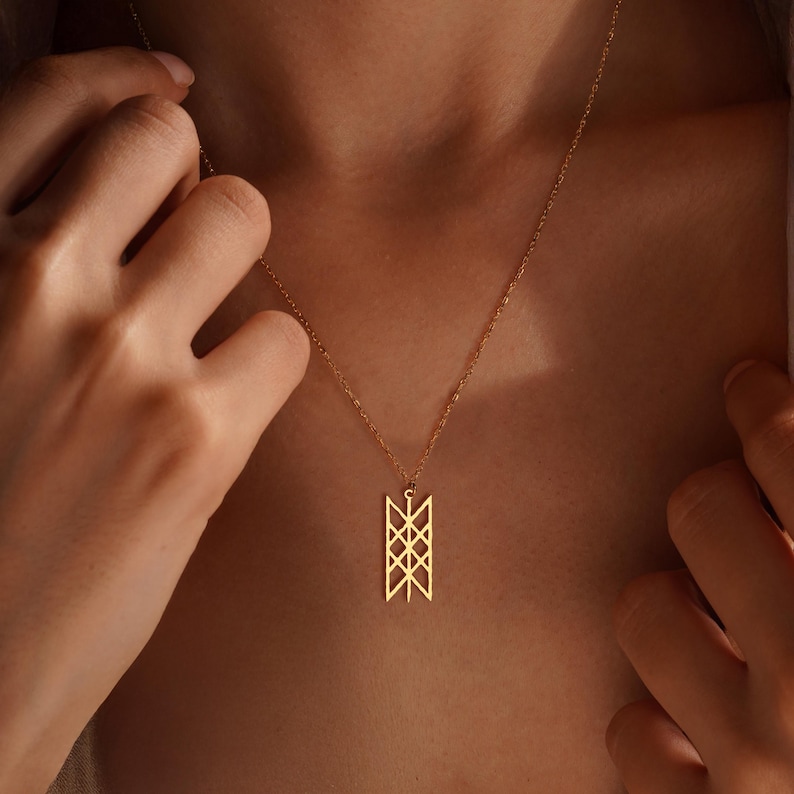 May include: A gold pendant necklace with a geometric design. The pendant is rectangular with intersecting lines and shapes. The necklace is worn around the neck. The pendant's design is approximately 2.5 cm in length.