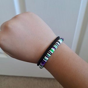 Pu&ograve; includere: Due braccialetti su un polso. Un braccialetto &egrave; nero e l'altro &egrave; bianco, verde e viola.
