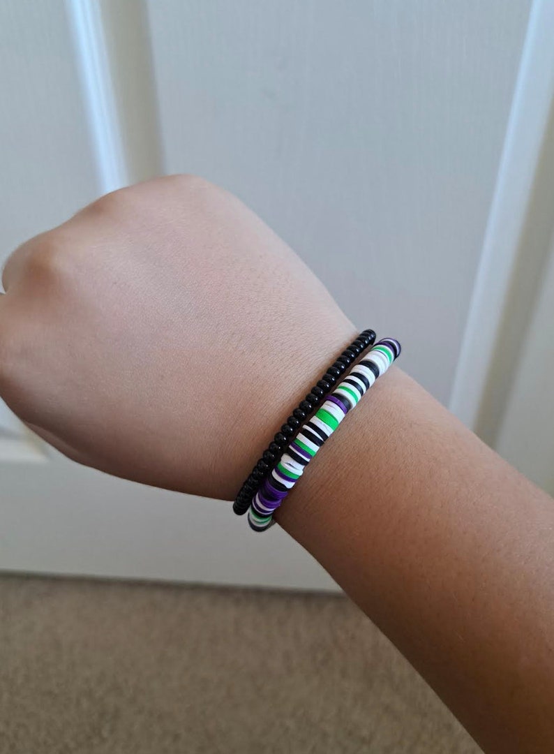 Pu&ograve; includere: Due braccialetti su un polso. Un braccialetto &egrave; nero e l'altro &egrave; bianco, verde e viola.