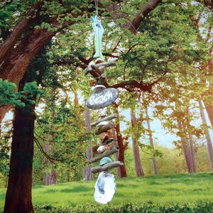 May include: A beach-themed wind chime hanging from a tree branch. The chime features a wooden sign with "Beach" written on it, along with shells, driftwood, and a large, clear crystal. The background shows a lush green forest.