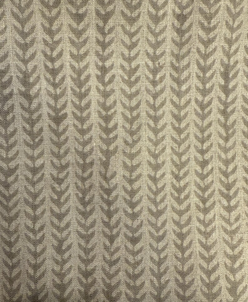May include: A close-up of a fabric with a repeating pattern of stylized, light brown leaf shapes. The leaves are arranged in vertical rows against a beige background, creating a textured, natural look.