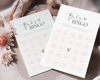 May include: Two white baby shower bingo cards with black text and a pink heart. The text on the cards reads "Baby Bingo". The cards have a grid of squares with baby-related words like "socks", "diaper", "bottle", and "blanket".