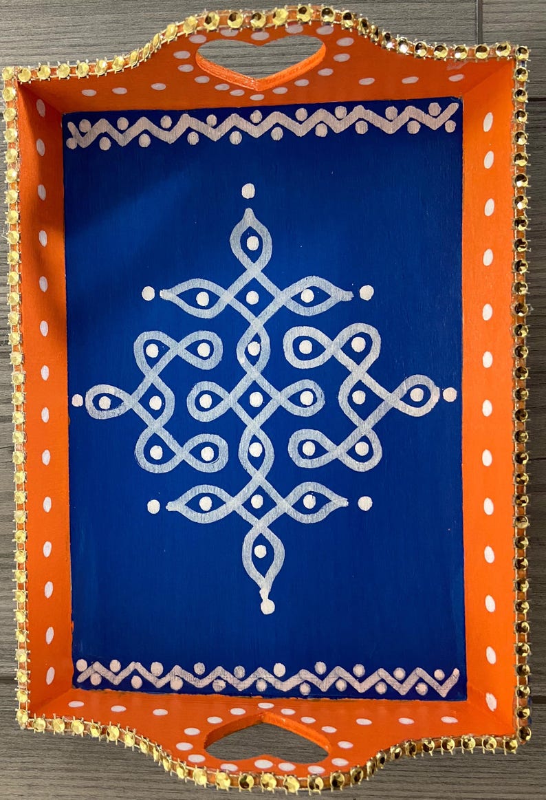May include: A wooden serving tray with a blue interior and orange exterior. The tray has a white geometric design painted on the blue surface and a white polka dot pattern on the orange surface. The tray has a gold trim around the edges.