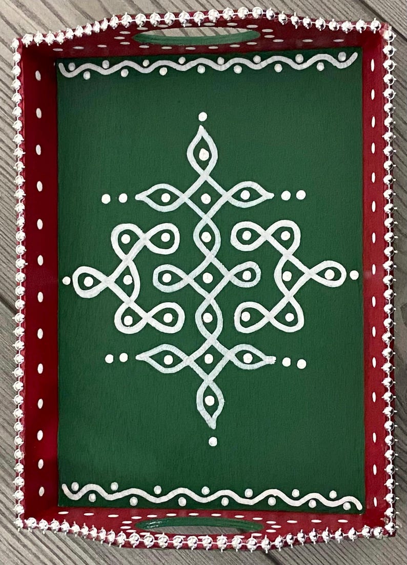May include: A green wooden tray with a white geometric design painted on the surface. The tray has a red border with white dots and a silver beaded trim.