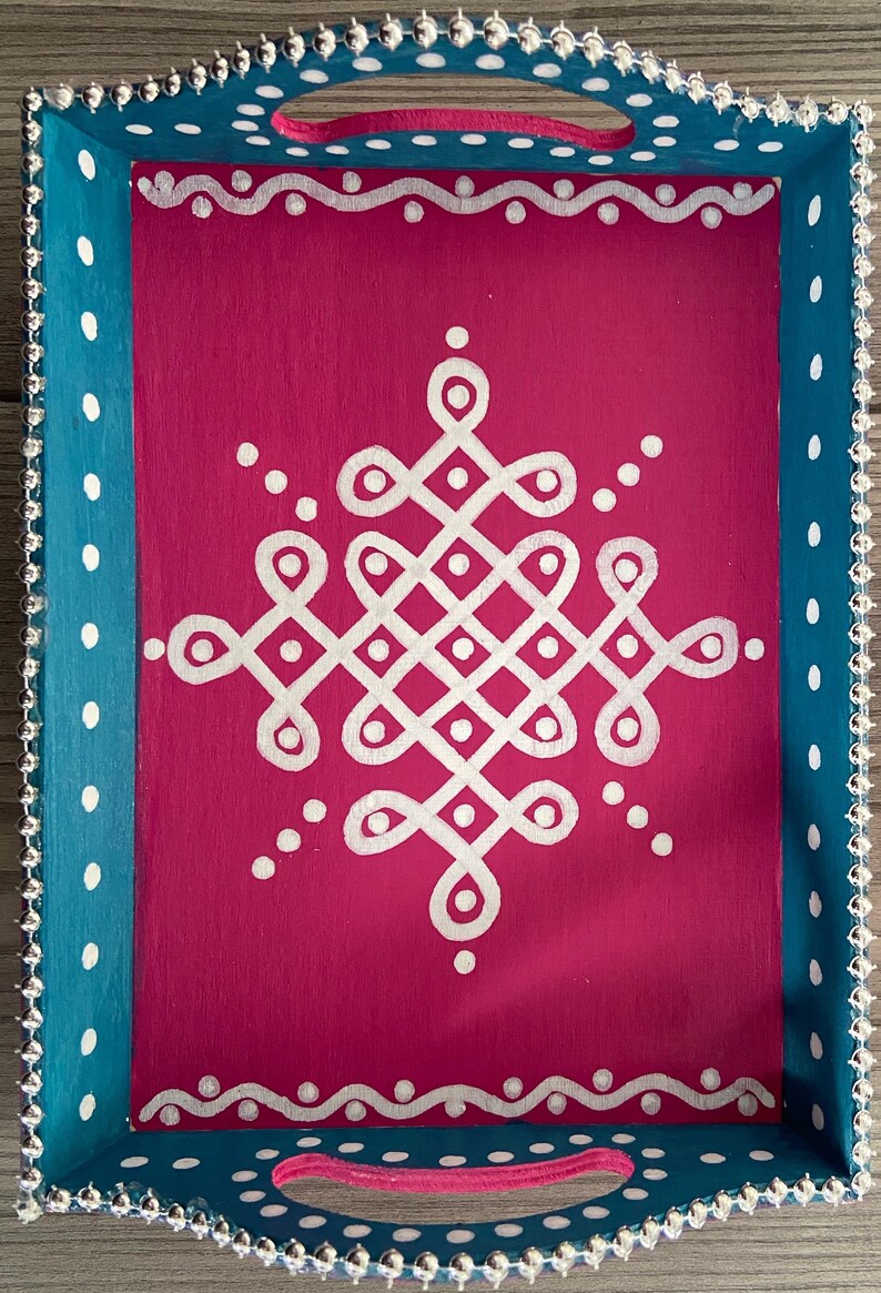 May include: A teal and pink wooden serving tray with white polka dots and a white geometric design in the center. The tray has silver beaded trim around the edges.