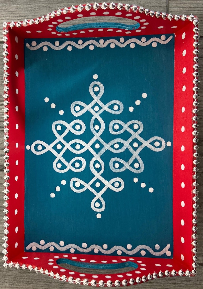 May include: A teal wooden tray with a white geometric design painted on the surface. The tray has a red border with white polka dots and a silver beaded trim.