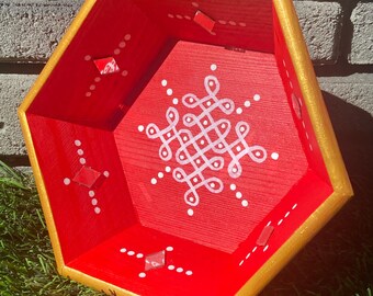 May include: A red hexagonal wooden bowl with a gold rim. The bowl has a white geometric design painted on the inside. The bowl is sitting on a green grassy surface.