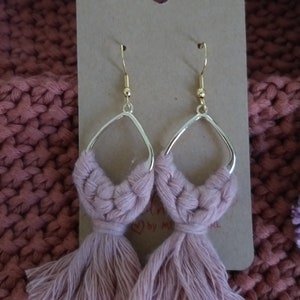 May include: A pair of pink tassel earrings with gold hoops. The earrings are handmade and have a bohemian style.