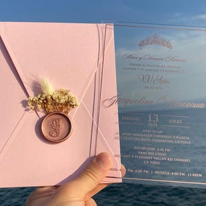 Pode incluir: Um convite de Quincea&ntilde;era rosa e ouro rosa com uma sobreposi&ccedil;&atilde;o de acr&iacute;lico transparente. O convite apresenta o texto "Hares y Verenica Amereva" e "Jacqueline Amereva". O convite inclui a data e hora do evento, bem como a localiza&ccedil;&atilde;o da igreja e da recep&ccedil;&atilde;o.