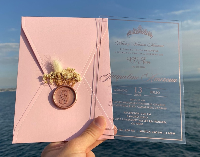 Pode incluir: Um convite de Quincea&ntilde;era rosa e ouro rosa com uma sobreposi&ccedil;&atilde;o de acr&iacute;lico transparente. O convite apresenta o texto "Hares y Verenica Amereva" e "Jacqueline Amereva". O convite inclui a data e hora do evento, bem como a localiza&ccedil;&atilde;o da igreja e da recep&ccedil;&atilde;o.