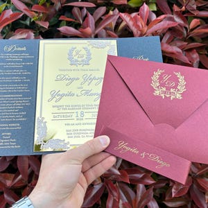May include: A wedding invitation suite featuring a navy blue card with details, a gold and cream invitation, and a burgundy envelope. The invitation includes the names Diego Yopoz and Yogita Mangal, and the date of the wedding.