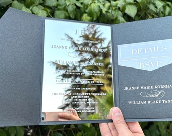 Könnte beinhalten: Eine dunkelgraue Hochzeitseinladung mit reflektierender Oberfläche, mit den Namen Jeanne Marie Kornhardt und William Blake Tanner. Die Einladung enthält Details und RSVP-Karten in einer Tasche, mit Datum und Ort der Hochzeit.