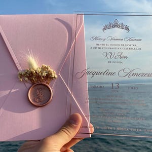 Pode incluir: Convite rosa e transparente para uma Quincea&ntilde;era, com uma coroa dourada e o texto "Marco y Veronica Amezcua TIENEN EL HONOR DE INVITAR A USTED Y SU FAMILIA A CELEBRAR LOS XV A&ntilde;os DE SU HIJA Jacqueline Amezcua S&Aacute;BADO 13 2024 JULIO"