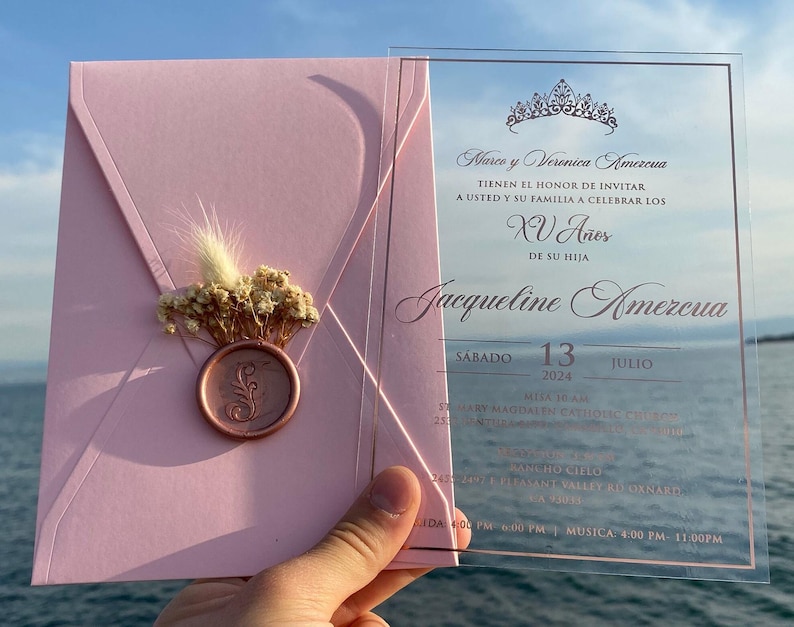 Pode incluir: Convite rosa e transparente para uma Quincea&ntilde;era, com uma coroa dourada e o texto "Marco y Veronica Amezcua TIENEN EL HONOR DE INVITAR A USTED Y SU FAMILIA A CELEBRAR LOS XV A&ntilde;os DE SU HIJA Jacqueline Amezcua S&Aacute;BADO 13 2024 JULIO"