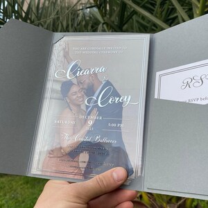 May include: A wedding invitation with a clear plastic cover. The invitation is for Cicarra and Corey's wedding on December 9, 2023 at 5:00 PM at The Crystal Ballroom. The invitation features a photo of the couple.