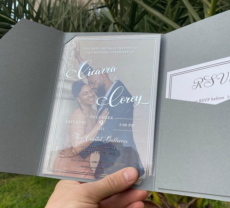 May include: A wedding invitation with a clear plastic cover. The invitation is for Cicarra and Corey's wedding on December 9, 2023 at 5:00 PM at The Crystal Ballroom. The invitation features a photo of the couple.