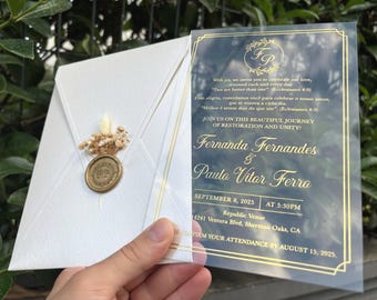 May include: A clear acrylic wedding invitation with gold foil text featuring the names Fernanda Fernandes and Paulo Vitor Ferro, paired with a white envelope sealed with a gold wax seal and decorated with small dried flowers and grasses.