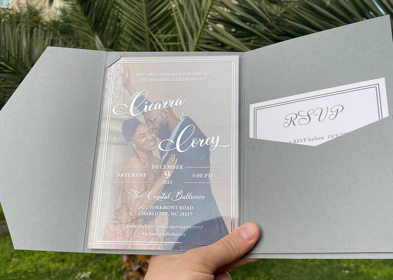 May include: A wedding invitation with a photo of the couple, Ciearra and Corey, on a clear background. The invitation is for a wedding ceremony on December 9th, 2023 at 5:00 PM at The Crystal Ballroom, 2421 Yorkmont Road, Charlotte, NC 28217. The RSVP deadline is 10/5/2023.