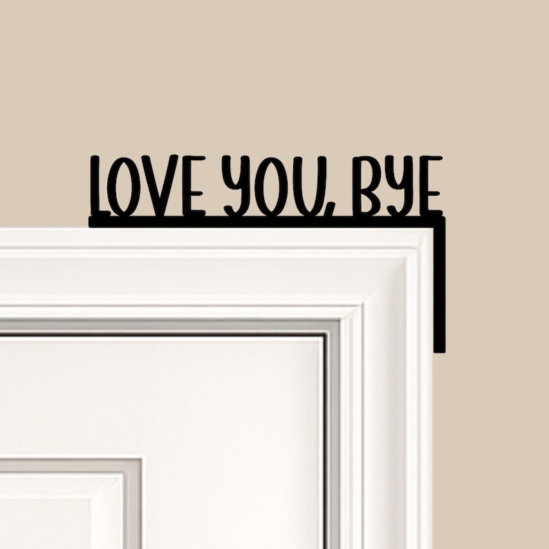 Black wood L-shaped door-corner signs reading “LOVE YOU, BYE” in bold letters. The Small version measures 10-3/4" wide × 6" tall, and the Large version measures 17-1/4" wide × 7-3/8" tall. Both are 1/4" thick and designed to perch on a door-frame corner without installation hardware.