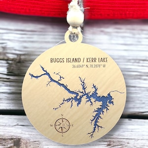 May include: A wooden ornament with a blue outline of Buggs Island / Kerr Lake, North Carolina. The ornament includes the coordinates 36.6049° N, 78.2878° W and a compass rose.