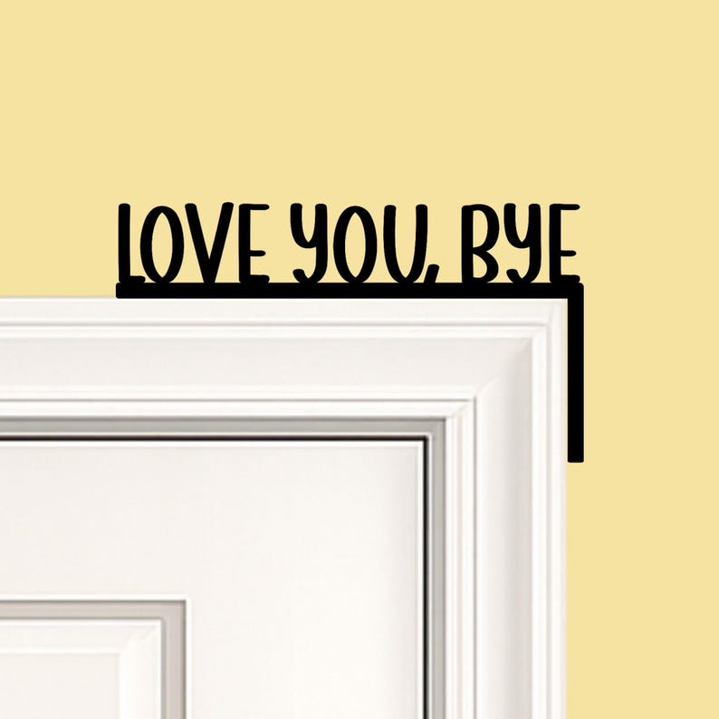 Black wood L-shaped door-corner signs reading “LOVE YOU, BYE” in bold letters. The Small version measures 10-3/4" wide × 6" tall, and the Large version measures 17-1/4" wide × 7-3/8" tall. Both are 1/4" thick and designed to perch on a door-frame corner without installation hardware.