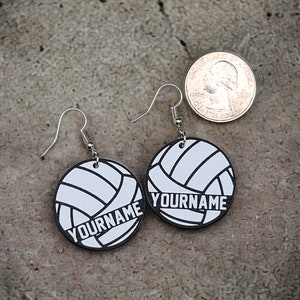 May include: A pair of silver earrings with a white volleyball design and the text "YOURNAME" on each earring.