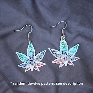 May include: A pair of silver dangle earrings with a colorful tie-dye mandala design in the shape of a marijuana leaf.