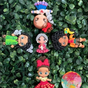 May include: Set of six handmade clay figurines, featuring characters from various cultures. The figurines are colorful and detailed, with expressive faces and intricate clothing. The figurines are displayed on a bed of green foliage.