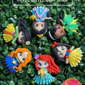 Puede incluir: Seis figuritas de arcilla hechas a mano de princesas Disney. Las princesas son Blancanieves, Cenicienta, Ariel, Bella, Pocahontas y Mulan. Cada figurita lleva un vestido diferente y tiene un peinado único. Las figuritas están todas mirando hacia adelante y están dispuestas en círculo.