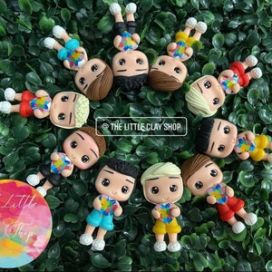 Puede incluir: Un conjunto de 10 figuritas de arcilla de colores de personas que sostienen piezas de rompecabezas en forma de corazón. Las figuritas llevan ropa de diferentes colores y tienen diferentes peinados. El texto "@THE LITTLE CLAY SHOP" es visible en la imagen.