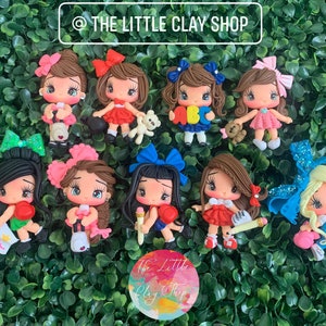 Puede incluir: Una colección de diez muñecas de arcilla polimérica hechas a mano con diferentes peinados, atuendos y accesorios. Las muñecas llevan todas vestidos de diferentes colores y tienen el pelo de diferentes colores. Algunas de las muñecas sostienen objetos, como un libro, un lápiz y un osito de peluche. Las muñecas sonríen todas y tienen ojos grandes.