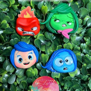 Puede incluir: Cuatro cabezas de personajes de arcilla hechas a mano de la película Del revés. Los personajes son Ira, Desagrado, Alegría y Tristeza. Cada personaje está pintado en su color respectivo y tiene una expresión única.