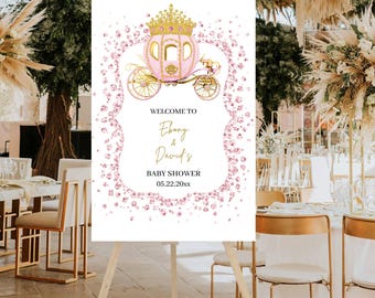 Puede incluir: Un letrero de bienvenida para un baby shower sobre un caballete. El letrero presenta una ilustración de un carruaje rosa y dorado con una corona. El texto dice "Welcome to Ebony & David's Baby Shower 05.22.20xx". El letrero está rodeado de acentos florales rosas.