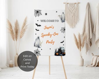 Könnte beinhalten: Ein rechteckiges weißes Willkommensschild auf einer Holzstaffelei mit Halloween-Grafiken wie Geistern, schwarzen Fledermäusen, Spinnennetzen und einem Spukhaus mit Kürbissen. Der Text lautet: WELCOME TO Jason's Spooky-One Party.